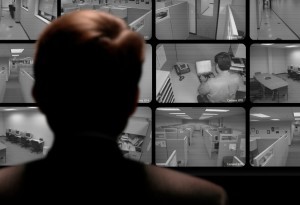 Man watching an employee work via a closed-circuit video monitor